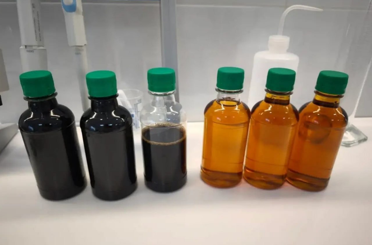 Six laboratory bottles on a lab bench: three holding dark humic-acid extract alongside three holding amber fulvic-acid extract.